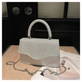 Silver evening bag with sparkling rhinestones on handle and flap next to a magazine - Silver