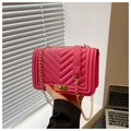Macro shot of fuchsia quilted handbag with V-stitch texture and gold metal chain strap - Pink