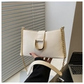 Close-up of cream leather shoulder bag featuring a large gold D-ring buckle and chain strap - White