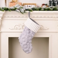 Gray knitted Christmas stocking with white cuff hanging on a festive white fireplace - Gray