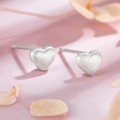 Dettaglio macro di orecchini a cuore satinati su sfondo floreale rosa tenue - Orecchini a cuore spazzolato / Piccolo
