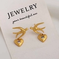 Macro shot of gold bird earrings with heart zircon pendants on a jewelry card - Gold