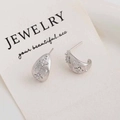 Macro shot of silver C-shaped earrings with brushed metal finish and zircon clover detail - C-Shape Stud Earrings / Silver