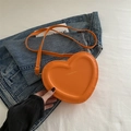 Orange heart-shaped crossbody bag in matte leather finish on denim background - Orange