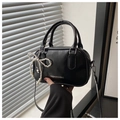 Detail of glossy black handbag with pearl bow charm and elegant hand-held strap - Black