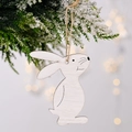 White wooden Easter bunny ornament with jute string hanging on snowy pine branch - White