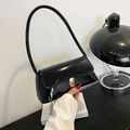 Chic black patent leather shoulder bag with gold metal buckle held by model - Black