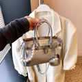 Chic silver metallic Kelly bag with pearl strap and heart charm in a hand-held view - Heart Charm Style / Silver
