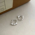 Macro detail of silver knot hoop earrings with a high-polished finish on textured paper - Silver Polished Knot Huggie (EH775)