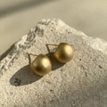 Detailed macro shot of matte gold pebble shaped earrings on a natural textured stone - Gold