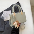 Bolso verde menta con asa trenzada y colgante de caballo sobre una chaqueta de traje - Verde