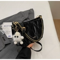 Detail van zwarte geplooide crossbodytas met gouden ketting en wit pluchen monstertje - Gerimpelde textuur / Zwart