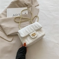 White quilted rectangular chain crossbody bag with gold-tone hardware on a beige blazer - White