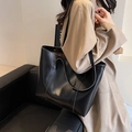Minimalist black tote bag in smooth leather finish worn by a model in a beige trench coat - Black