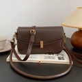 Vintage dark brown leather shoulder bag with gold metal buckle on a retro book - Coffee