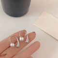 Detail of silver U-shaped pearl earrings featuring water drop pendants held by hand - White Gold