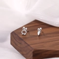 Macro shot of asymmetric S925 silver rabbit and carrot earrings on a dark walnut block - Rabbit Carrot Stud Earrings - Platinum Color