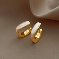 Detailed view of gold rectangular huggie earrings with white enamel inlay on beige stand - White