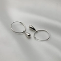Detail von silbernen Tropfenohrringen mit geometrischen Ringen auf weißer Seide - Minimalistische Tropfenohrringe / Silber