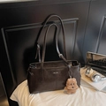 Détail d'un sac à bandoulière en cuir marron foncé avec logo métallique et pendentif ours - Avec Pendentif / Café