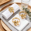 Set of three gold mimosa leaf napkin rings on white linens with natural wood decor - Mimosa Leaf / Gold