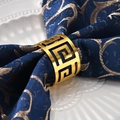 Close-up of golden hollow greek meander napkin ring on a blue fabric napkin - Gold Greek Key