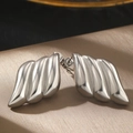 Primer plano de pendientes plateados con forma de ala sobre una elegante seda color champán - Estilo de Ala de Ola Plateada (C2232)