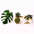Macro detail of gold tropical napkin rings with pineapple, monstera leaf and palm tree designs - Monstera Leaves