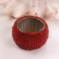 Rond de serviette artisanal avec perles de verre rouges et fil doré sur socle foncé - Rouge