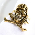 Golden pirate skull and crossbones napkin ring with detailed metal carving on white linen - Skull