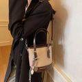 Borsa a secchiello retrò in pelle beige e marrone scuro indossata a tracolla dalla modella - Con Ciondolo / Cachi