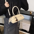Beige cylindrical baguette bag with metallic rivets and brown charm on a model's shoulder - With Pendant / White