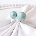Macro shot of mint green dual pearls on golden ring set on white silk fabric - Teal Blue