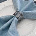 Modern geometric hollow gunmetal napkin ring on light blue linen napkin and white ceramic plate - Black Hollow Grid Napkin Ring