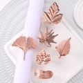 Rose gold leaf napkin rings set with various plant designs on a white tray - Rose Gold