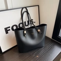 Minimalistische schwarze Shopper-Tasche mit Goldlogo und Metallringen auf Holzgrund - Schwarz