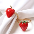 Golden napkin rings with red enamel strawberry charms set on white fabric - Gold
