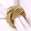 Macro shot of hand-woven champagne gold knot napkin ring on a white fabric napkin - Golden Woven Napkin Ring