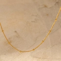 Dettaglio di una collana girocollo minimalista con perline d'oro su marmo liscio - Oro (C4403)
