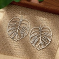 Detail shot of hollow monstera leaf earrings on rustic burlap with natural greenery - Silver Style (C6160)