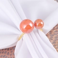 Luxurious gold napkin ring with two pink pearls on elegant white folded fabric - Coral Orange Double Pearl (R-004)