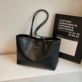 Large black faux leather tote bag with long straps and metal logo on marble surface - Black