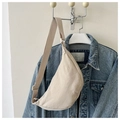 Detail of a beige crescent crossbody bag against a denim jacket backdrop - Beige