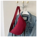 Side view of a burgundy crescent crossbody bag hanging on a denim jacket. - Red