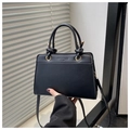 Detail of a black leather handbag featuring golden metal buckles and vintage embossed text - Black