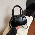 Glossy black bowling handbag with top handles and detachable strap on a white fur rug - Black