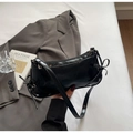 Vue à plat du sac d'épaule noir brillant avec nœuds et rivets sur un blazer gris - Noir