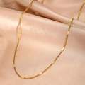 Dettaglio di una catena in acciaio inossidabile dorato su fondo di raso champagne - Collana con piastra metallica minimalista dorata (B9435)