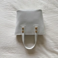 Elegante bolso de cuero blanco con remaches dorados y forma trapezoidal minimalista - Blanco