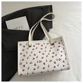 Detail of white tote bag with red cherry print and golden metal buckles on shoulder straps - White